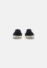 Sorte kanvas-sneakers med snøring, gummisåle og hvit tåhette. "Converse All Star" trykt på hælen. Enkelt og lavt design.