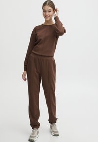 Brun sweatshirt och joggers-set tillverkat i ett mjukt material, med avslappnad passform, elastisk midja och ribbade ärmslut. Sneakers ingår.