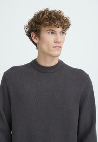 Temno siva pletena jopica z okroglo izrezom, dolgimi rokavi in mehko teksturo. Preprost dizajn brez vidnih vzorcev ali dodatkov iz kovine.