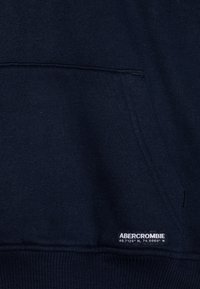 Felpa blu navy realizzata in un morbido tessuto testurizzato, con tasca frontale, polsini a coste e un logo ricamato con le coordinate.