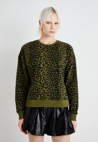 Felpa verde con stampa leopardata nera, colletto a girocollo a coste e polsini. Abbinata a una gonna plissettata in pelle nera. Tocco liscio.