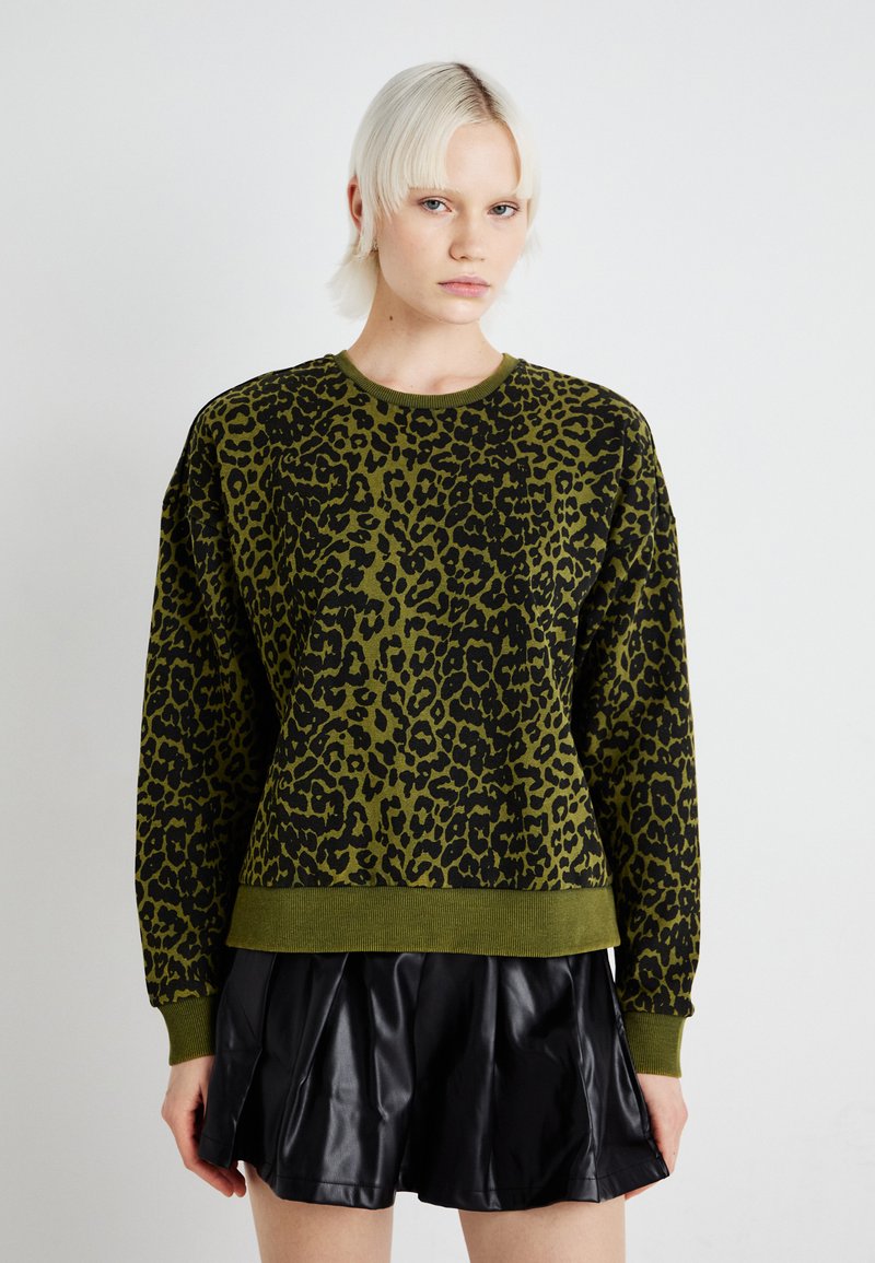 Felpa verde con stampa leopardata nera, colletto a girocollo a coste e polsini. Abbinata a una gonna plissettata in pelle nera. Tocco liscio.
