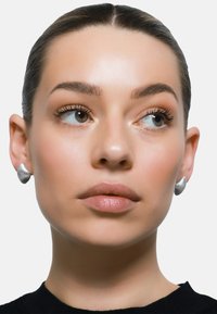 Orecchini a perno argento con texture e design rigato, indossati da una persona con trucco neutro e un maglione nero, che presenta un aspetto semplice ed elegante.
