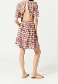 Bakvy av en kort klänning med volangärmar, utstansad rygg och ett flerfärgat diamantmönster i rosa, grönt och kräm. Kjolen har en utställd nederkant.