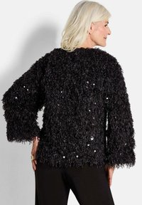 Schwarzer, kuscheliger Pullover mit langen Ärmeln, der eine strukturierte Oberfläche mit verstreuten Pailletten aufweist, was ihm ein auffälliges visuelles Detail verleiht.