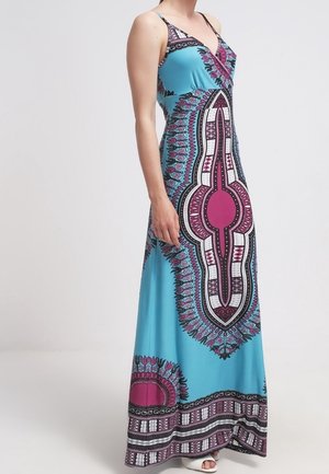 Kobieta w niebieskiej sukni bez rękawów sięgającej do podłogi z różowymi, białymi i czarnymi, misternymi geometrycznymi i kwiatowymi wzorami.