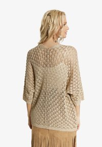 Stickad, öppen vävtröja i beige med lös passform, trekvartslånga ärmar och mönster i diamant. Strukturerad yta med ribbade kanter.