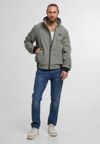 Graue Kapuzenjacke mit schwarzen Akzenten, Frontreißverschluss und Logo. Kombiniert mit blauen Jeans und weißen Turnschuhen, zeigt einen lässigen, entspannten Look.