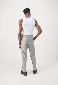 Grijze ribbroek met elastische tailleband en achterzak, gecombineerd met een witte tanktop. Het model staat met de rug naar de camera.