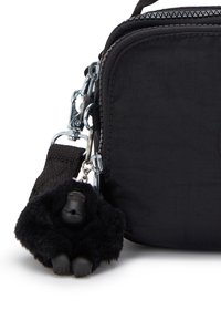 Borsa a tracolla nera in tessuto con chiusura a zip, dotata di un portachiavi a forma di gorilla nero texturizzato attaccato da un clip argentato.