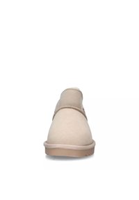 Scarpa beige in suede, senza lacci, con punta arrotondata, cuciture visibili e una morbida fodera interna; presenta una suola in gomma testurizzata.