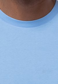 Helles blaues Baumwoll-T-Shirt mit rundem Ausschnitt, das eine glatte Textur und minimale Nahtdetails am Kragen aufweist.