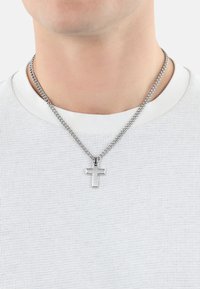 Collana in argento con pendente a croce di medie dimensioni e lucido, indossata sopra una camicia bianca con texture.