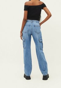 Pantalones cargo de denim azul de talle alto con piernas anchas, dos bolsillos laterales y dos bolsillos traseros, presentando una textura ligeramente deslavada.