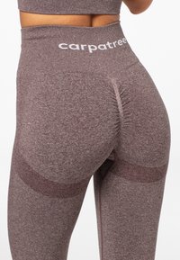 Leggings de tiro alto en una tela marrón texturizada y apagada. Presentan una costura fruncida en la parte posterior y acentos en contraste a lo largo de las piernas.
