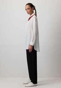 Witte lange mouwen blouse met een levendige rode versierde kraag, gecombineerd met zwarte wijde broekspijpen en witte schoenen. Eenvoudig, strak ontwerp.