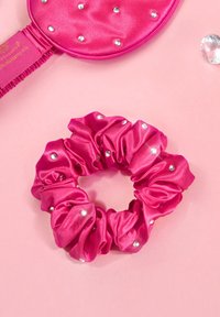 Różowa satynowa gumka do włosów o falistej fakturze i perłowymi akcentami, zaprezentowana na różowym tle, ilustrująca okrągły kształt.