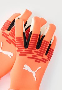 Orange målvaktshandskar med svarta detaljer, texturerat grepp på handflatan och vit loggdetalj. Tillverkade av andningsbart material, ergonomisk passform.