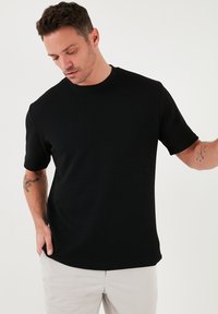 Schwarzes Kurzarm-T-Shirt aus strukturiertem Stoff mit rundem Ausschnitt, das eine lockere Passform und ein minimalistisches Design aufweist.