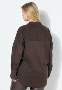 Camisa marrón abotonada con mangas largas con detalles de encaje, canesú trasero y corte holgado, confeccionada con una tela ligera.