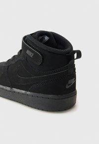 Svart Nike høyhælte sneakers med en glatt overdel, teksturerte detaljer, polstret krage og en gummisåle med Nike-logoen.