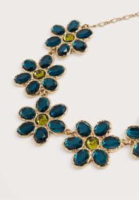 Zelta krāsas ziedu kaklarota, kas rotāta ar teal un zaļiem facētajiem dārgakmeņiem ar spīdīgu apdari. Katram ziedam ir centrālais akmens kontrastējošā krāsā.