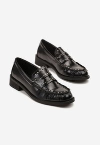 Mocassins en cuir noir avec des clous en argent le long de la sangle supérieure et de la zone des orteils, talon bas et bout arrondi, présentés sur un fond blanc.
