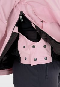 Rosa wasserdichte Jacke mit einem schwarzen Innenfutter, sichtbarem Reißverschluss und Druckknöpfen. Verfügt über einen elastischen Bund und Taschendetails.