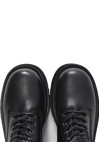 Černé kožené boty s kulatými špičkami, vybavené pevnými očky, šněrováním a texturovanou podrážkou. Hladký, lesklý povrch na svršku.