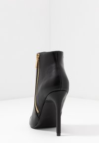 Stivale in pelle nera alla caviglia con tacco a stiletto alto, dotato di una cerniera dorata sul lato, finitura elegante e design della punta arrotondata.