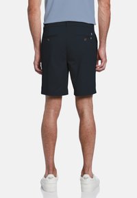 Marineblaue Shorts mit glatter Textur, ausgestattet mit Gesäßtaschen mit braunen Knöpfen und einem sauberen Saum. Kombiniert mit weißen Turnschuhen.