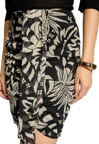 Jupe noire ornée d'un motif de feuilles et de fleurs en crème. Elle présente des détails drapés et une texture lisse. Accompagnée d'un bracelet doré.