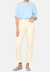 Ljusblå stickad tröja, krämfärgade raka byxor och blå lägenheter. Tröjan har korta ärmar; byxorna har hög midja och framfickor.