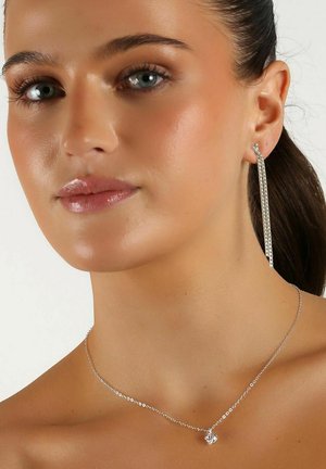 Silverhalsband med ett litet hjärtanhänge och ett par långa kedjeörhängen med en texturerad yta som hänger från örat.