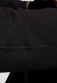 Personne portant un vêtement noir à manches longues, avec une mèche lâche de cheveux clairs visible près du cou.