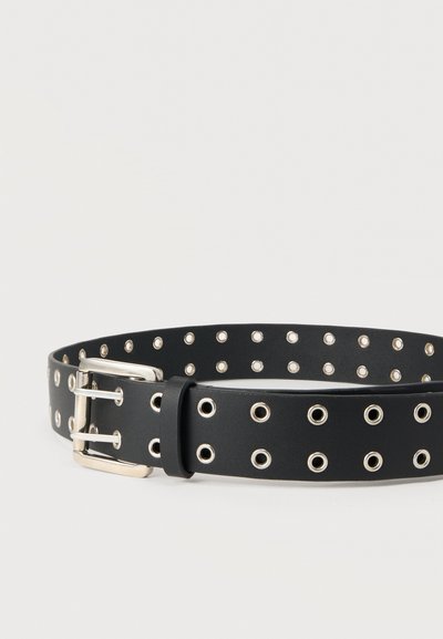 Μαύρη ζώνη από συνθετικό δέρμα με ασημένια πόρπη διπλής αγκράφας και ασημένιες τρύπες που είναι ομοιόμορφα τοποθετημένες σε όλο το μήκος της.