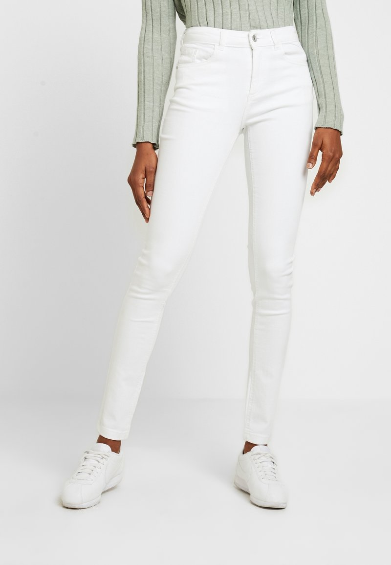 Vita smala jeans i denim med en mjuk textur. Har framfickor och knappstängning. Kombination med vita sneakers och en ljusgrön tröja.