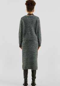 Grau gestricktes Sweater- und Rock-Set mit rundem Halsausschnitt, gerippten Abschlüssen und strukturierter Oberfläche, kombiniert mit schwarzen Stiefeln.