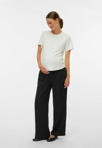 Porodniška obleka, ki vključuje kratkotrajno majico svetlo kremne barve ter hlače z visokim pasom in širokimi nogavicami v črni barvi z teksturirano tkanino.