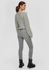Grijs geribbeld gebreid sweater met verlaagde schouders, gecombineerd met grijze skinny jeans. Zwarte enkellaarsjes hebben een dikke zool en een vetersluiting.