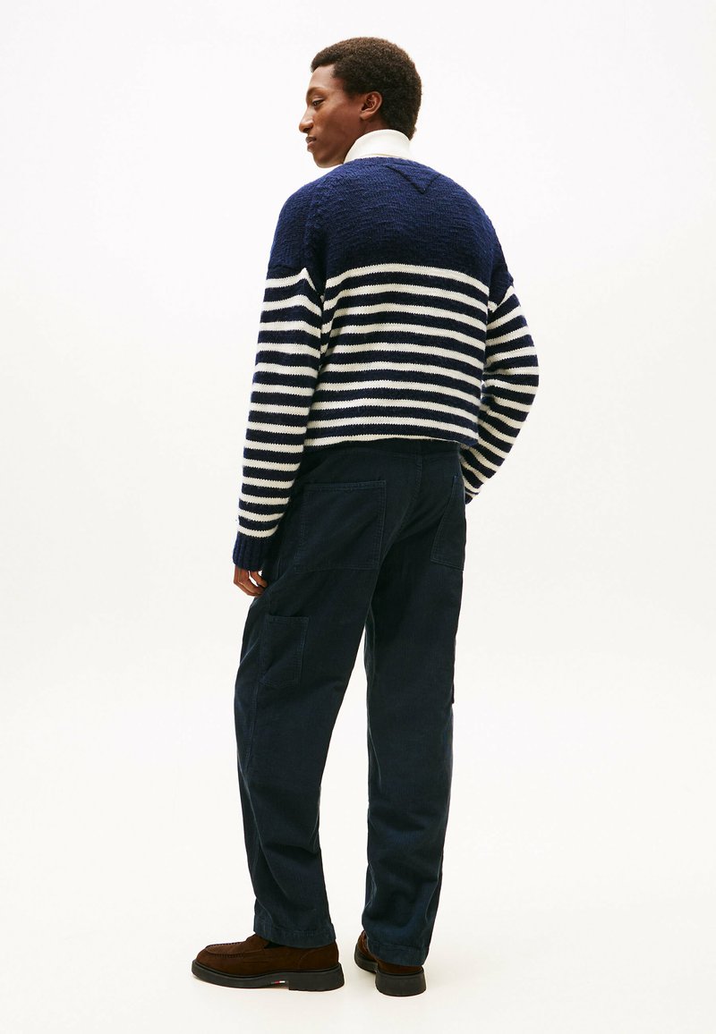 Navy and white striped knit sweater with a V-neck, paired with dark navy cargo pants and brown footwear. Shot from the back against a white background.