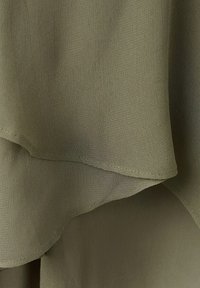 Gros plan sur un tissu vert olive à couches multiples avec une texture fine et des bords soigneusement cousus.
