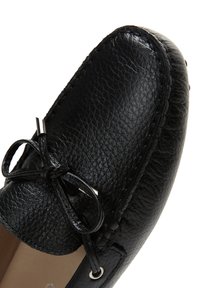 Mocasín negro de cuero con superficie texturizada, detalle de lazo y acentos metálicos. Punta redondeada y costuras contrastantes visibles.