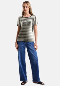 Stribet t-shirt i creme og sort, rund halsudskæring, korte ærmer, med et grafisk print. Sammen med vide jeans i blå og sorte sandaler.