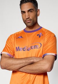 Tricou sport portocaliu cu textură de plasă, accente mov la guler și mâneci, și logo-ul "Mediacom" afișat proeminent.