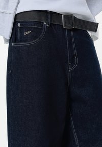 Mörkblå denimbyxor med klassisk passform, med kontrasterande sömmar och ett svart vävt bälte. Inkluderar framfickor och en logodetalj.