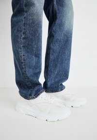 Hvite atletiske sneakers med teksturerte paneler og tykk såle, sammen med blå denimjeans med en falmet vask og rett ben-kutt.