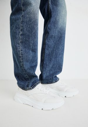 Weiße Sportsneakers mit strukturierten Einsätzen und einer dicken Sohle, kombiniert mit blauen Jeans aus Denim mit einer verblichenen Waschung und geradem Schnitt.