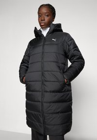 Svart vadderad puffjacka med dragkedja fram, huva och sidofickor. Har en quilted struktur och en liten vit logotyp på bröstet.