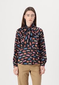 Svart bluse med fargerike bilmønstre, lange ermer og en halsbånd. Laget av glatt stoff med klassisk knappelukking foran.
